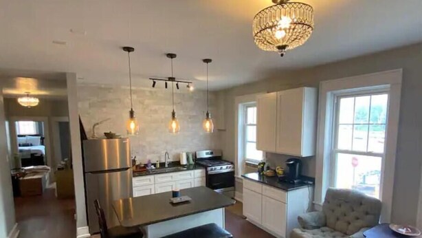 Una cocina moderna con una isla central, iluminación colgante y una araña.