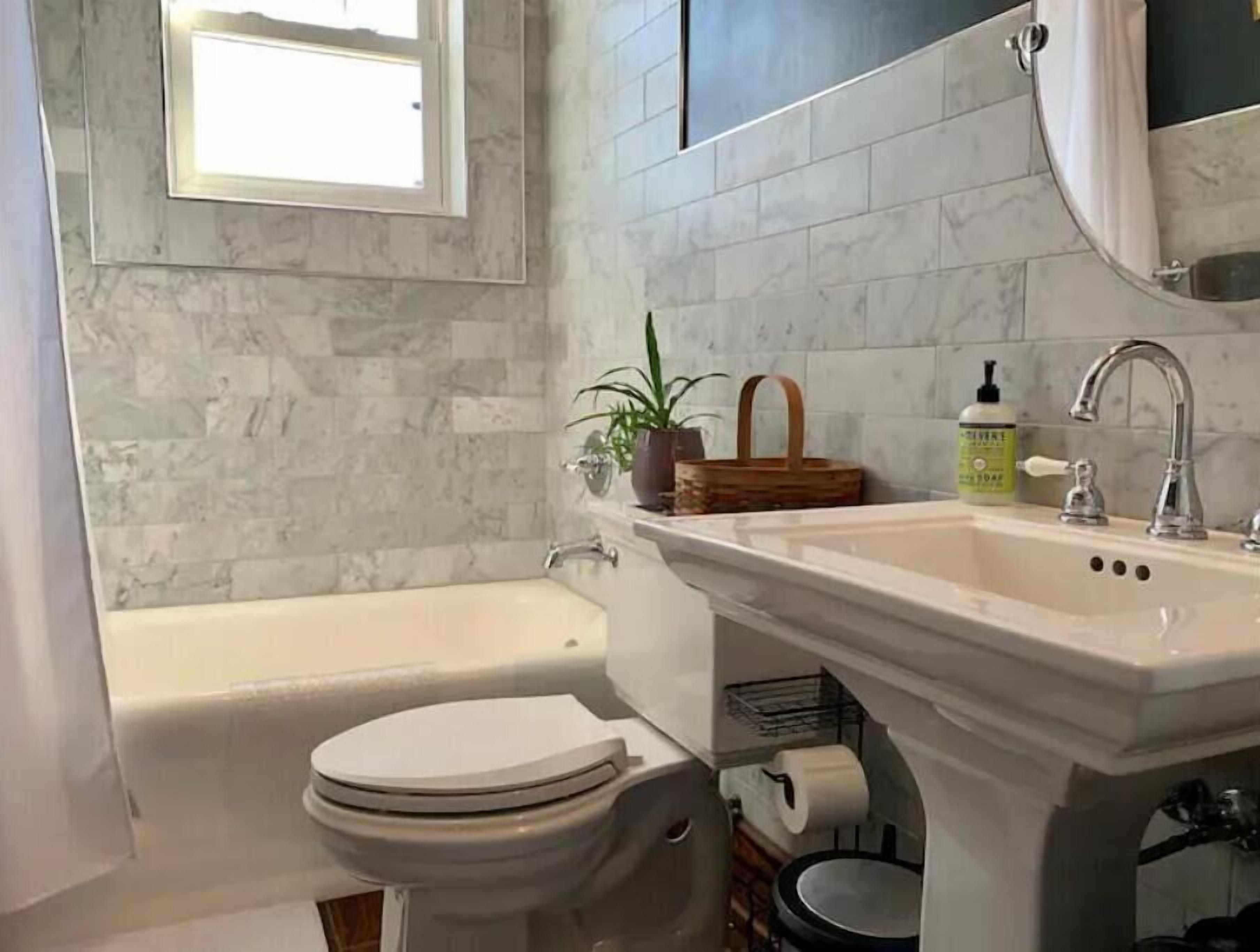 Un baño con bañera, inodoro, lavabo y una ventana sobre el inodoro.