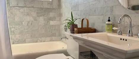 Un baño con bañera, inodoro, lavabo y una ventana sobre el inodoro.