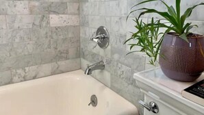Un baño con pared de azulejos de mármol, una bañera, un lavamanos y una planta en maceta.