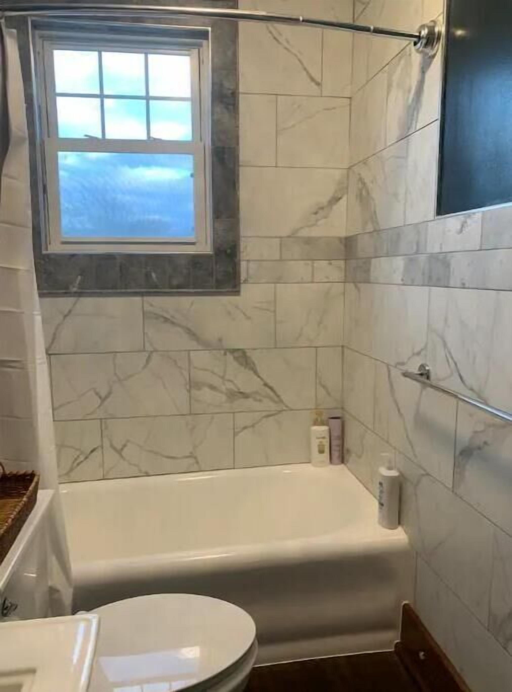 A bathroom with a bathtub, a toilet, and a window.