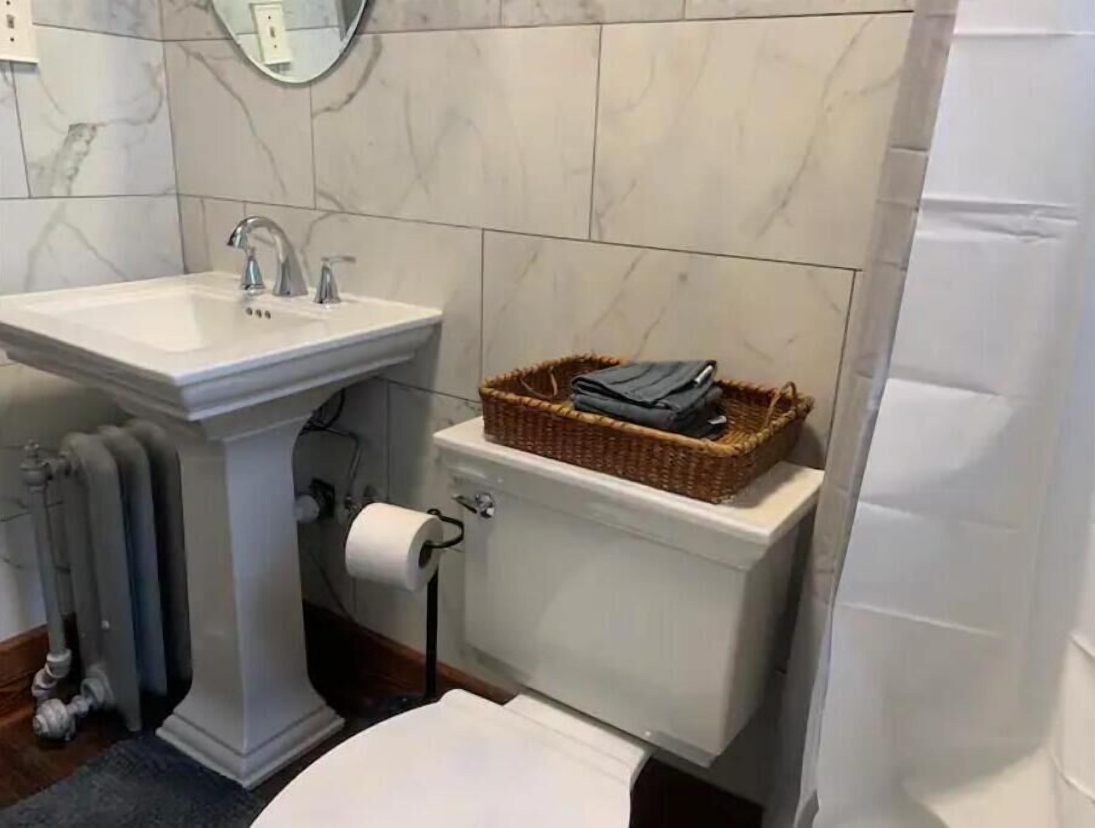 Un bagno con un lavandino su piedistallo, un WC con un cesto di articoli da toilette e un rotolo di carta igienica.