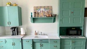 Une cuisine avec des armoires de couleur turquoise, un plan de travail blanc, une machine à café, un évier, un four à micro-ondes et un crédence décorative en carreaux.