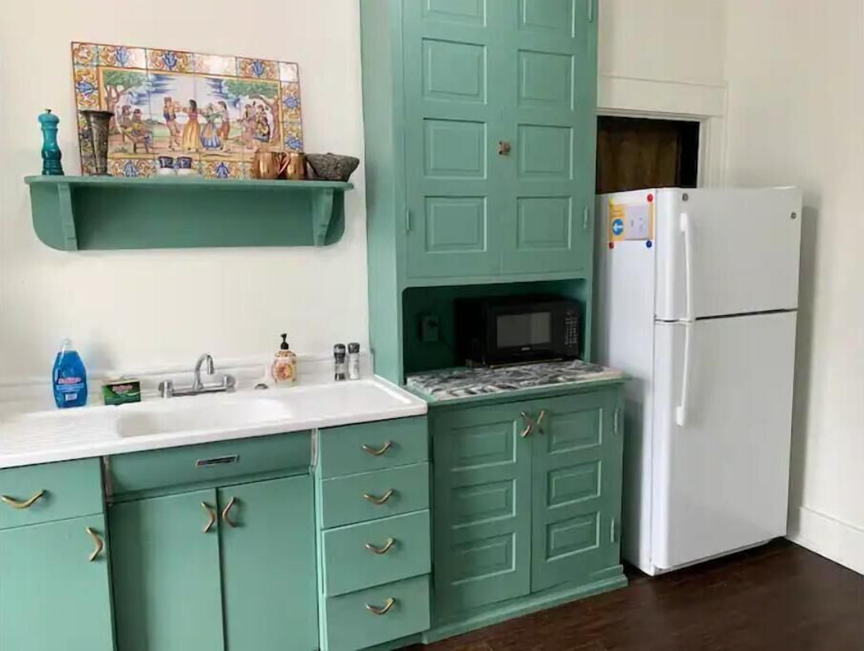 A kitchen with teal cabinets, a white sink, a microwave, and a white refrigerator.