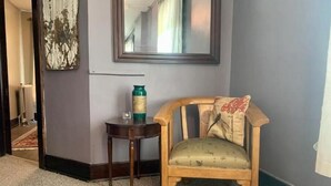 Un coin de pièce avec une chaise en bois, une petite table ronde surmontée d’un vase et un miroir accroché au mur.