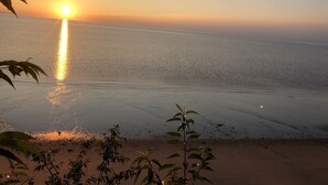 En strand med en solnedgång över vattnet, palmer i förgrunden och en klar himmel.