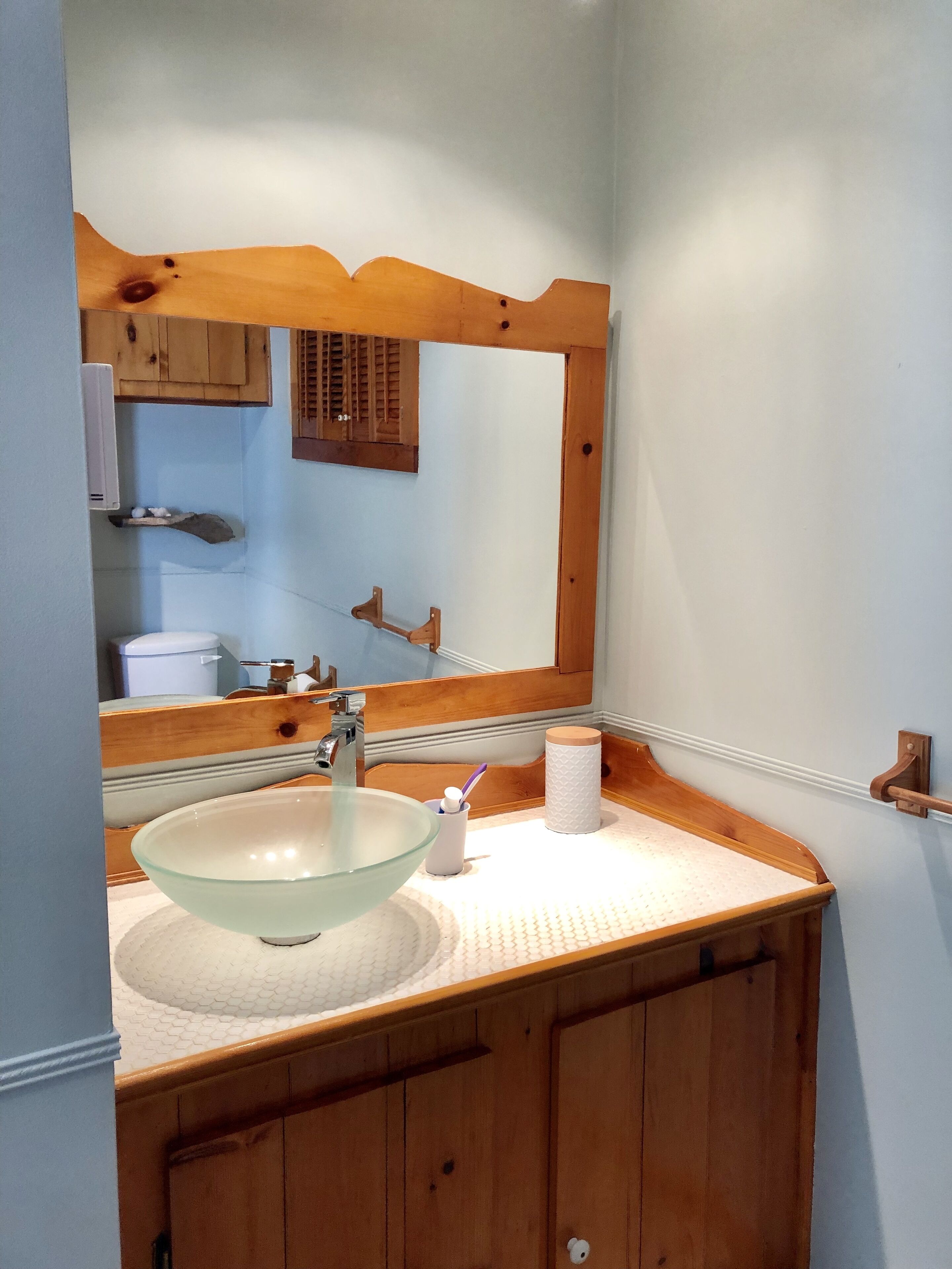 Un bagno con un mobile contenitore in legno, un lavabo in vetro, uno specchio e un erogatore di asciugamani.