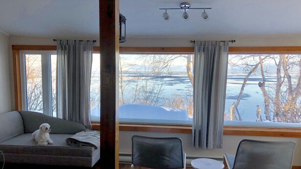 Ett rum med en soffa, två fåtöljer, ett litet bord och stora fönster med utsikt över en frusen sjö och träd.