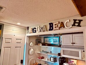 Une cuisine avec une porte blanche, un four à micro-ondes et une étagère contenant divers objets.