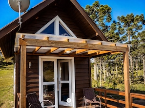 A wooden cabin with a covered porch, a satellite dish, and a view of pine trees.