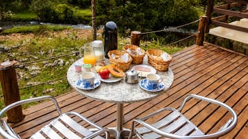 Mesa redonda con alimentos para el desayuno, dos sillas de metal y una terraza de madera con una barandilla de cuerda.
