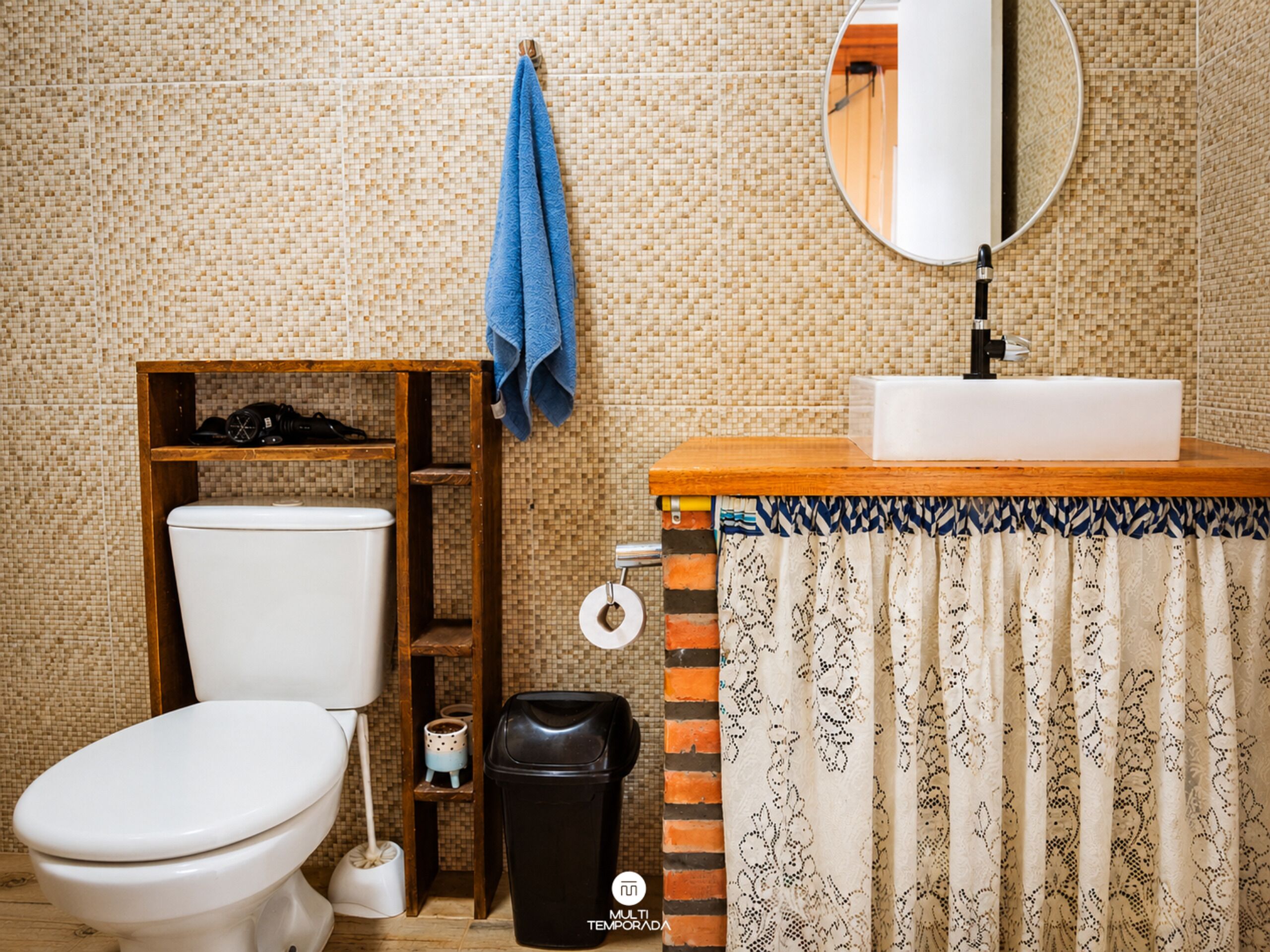 Une salle de bain comprenant des toilettes, une étagère avec des articles de toilette, une poubelle, une serviette accrochée au mur et un miroir.