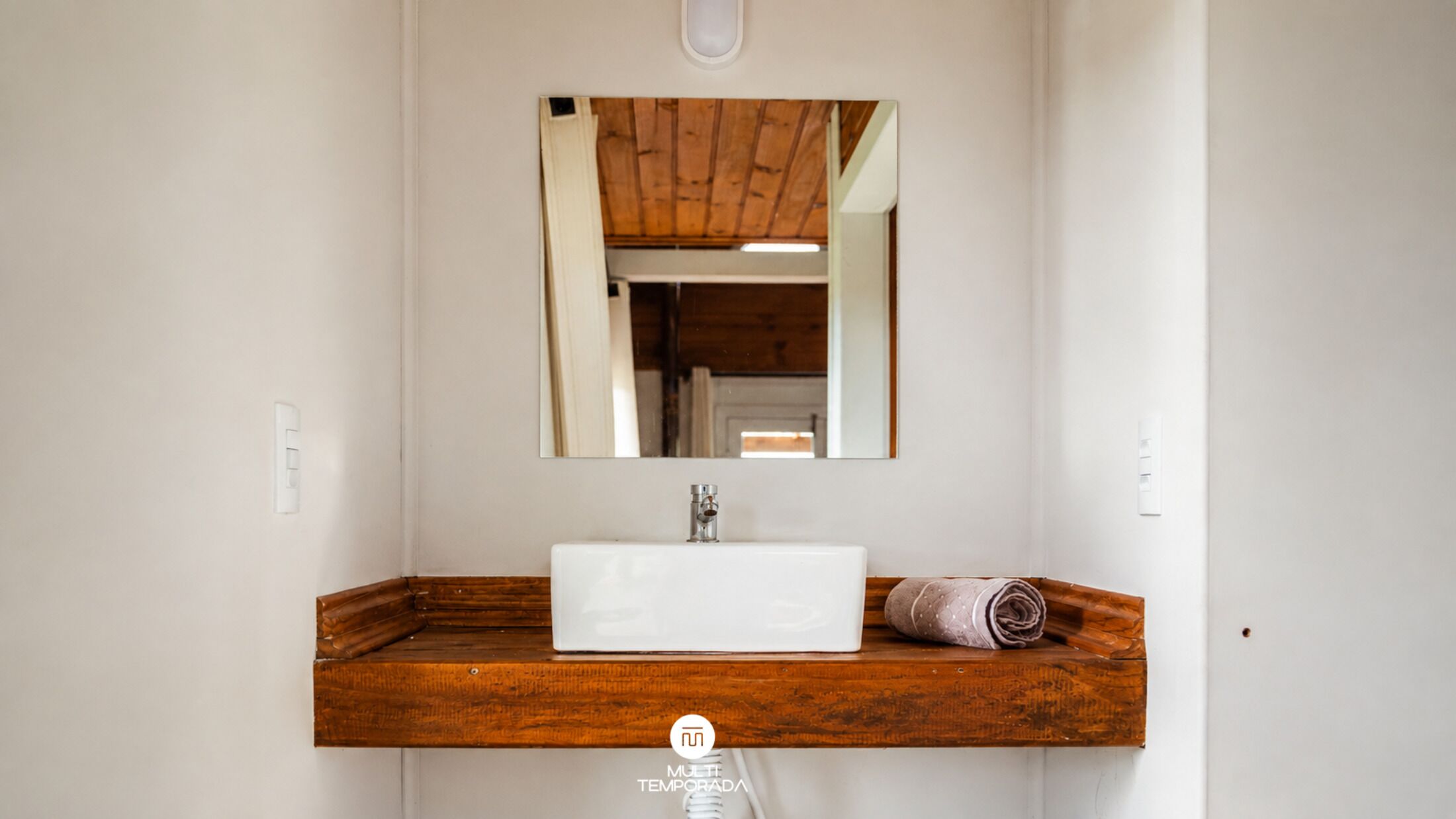 Une salle de bain avec un meuble-lavabo en bois, un lavabo blanc et un miroir au-dessus.