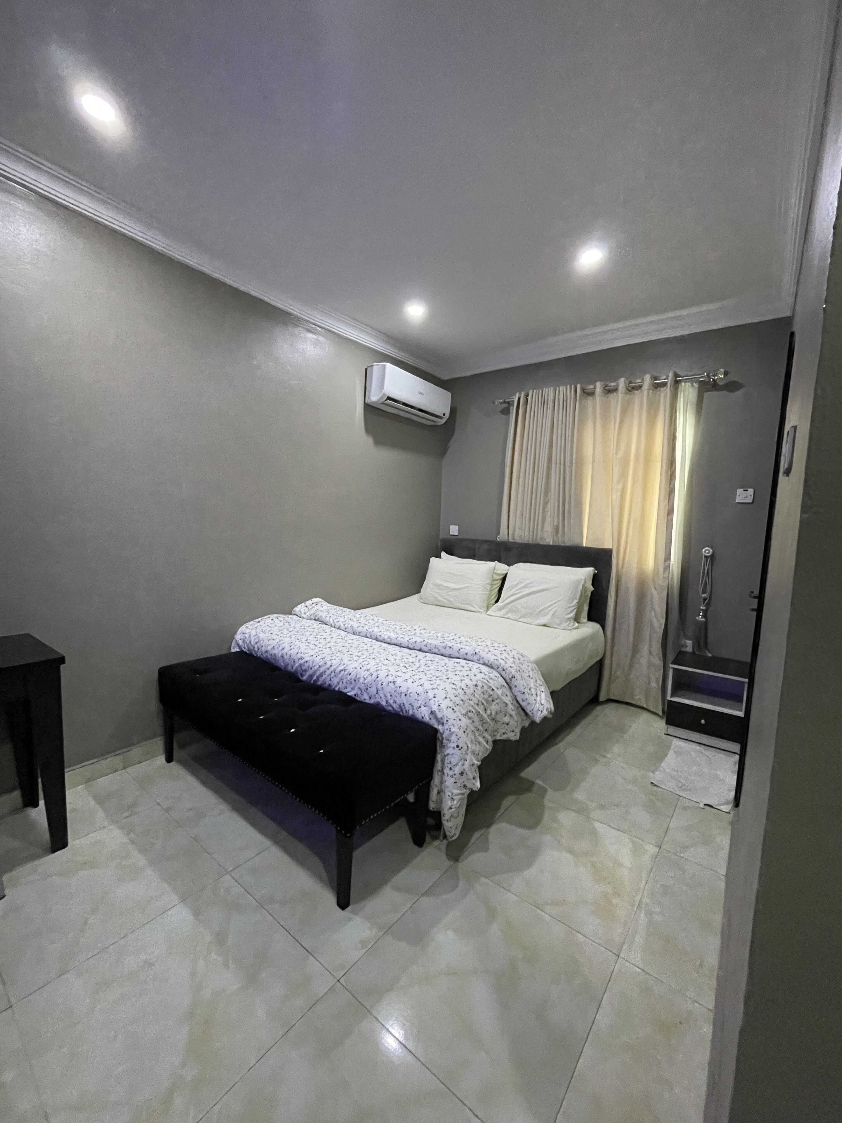 A bedroom with a bed, a bench, a wardrobe, and an air conditioning unit.