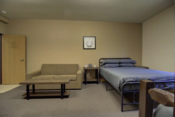 A small, neatly arranged room with a sofa, a single bed, a table, and a framed picture on the wall. - Legacy Lakeside Resort (Clitherall)