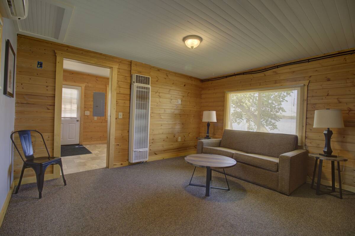 A cozy room with a wooden interior, a sofa, a small table, a chair, and a window with blinds.