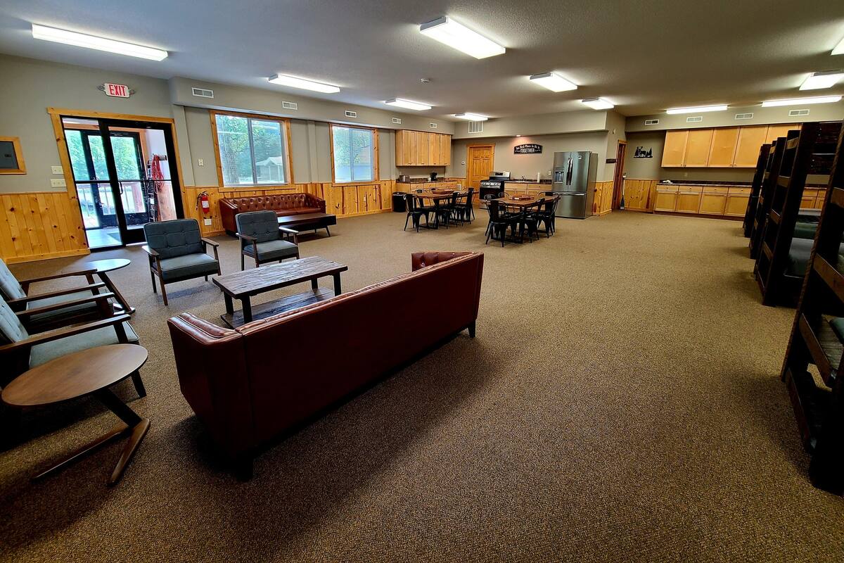 A spacious room with a red couch, multiple chairs, a wooden table, and a kitchen area with a refrigerator and cabinets.
