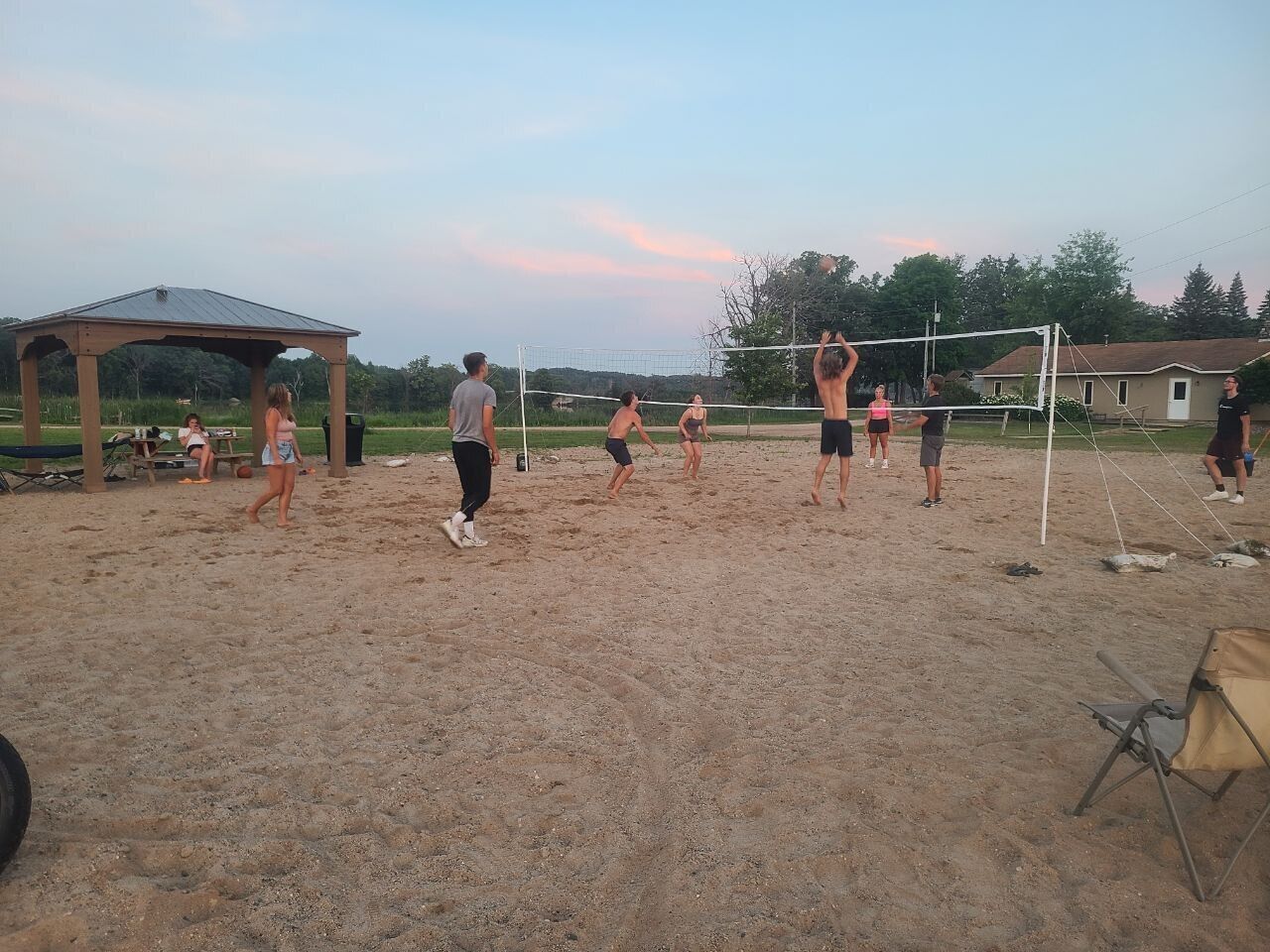 A volleyball game on a sandy court with a pavilion and houses in the background.