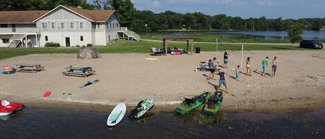 Una spiaggia con kayak e tavole da paddleboard, una zona riparata e una casa sullo sfondo.