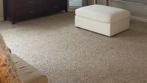 Un dormitorio con cómoda, reposapiés, tocador con espejo y un cuadro en la pared.