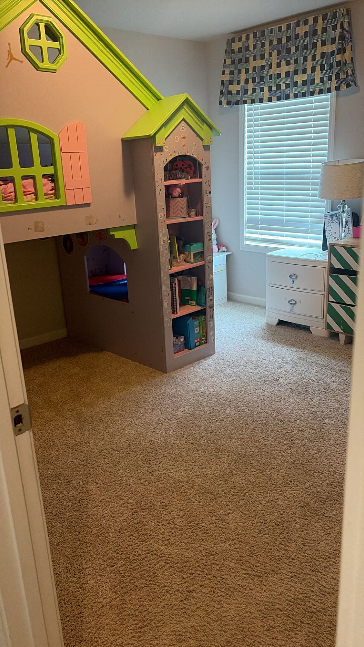 A child's playroom with a built-in bookshelf, a small desk, and a window with blinds.
