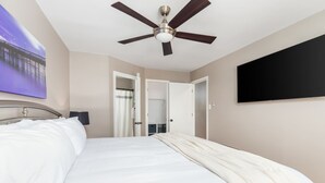Een hotelkamer met een bed, een plafondventilator, een televisie en een schilderij aan de muur.