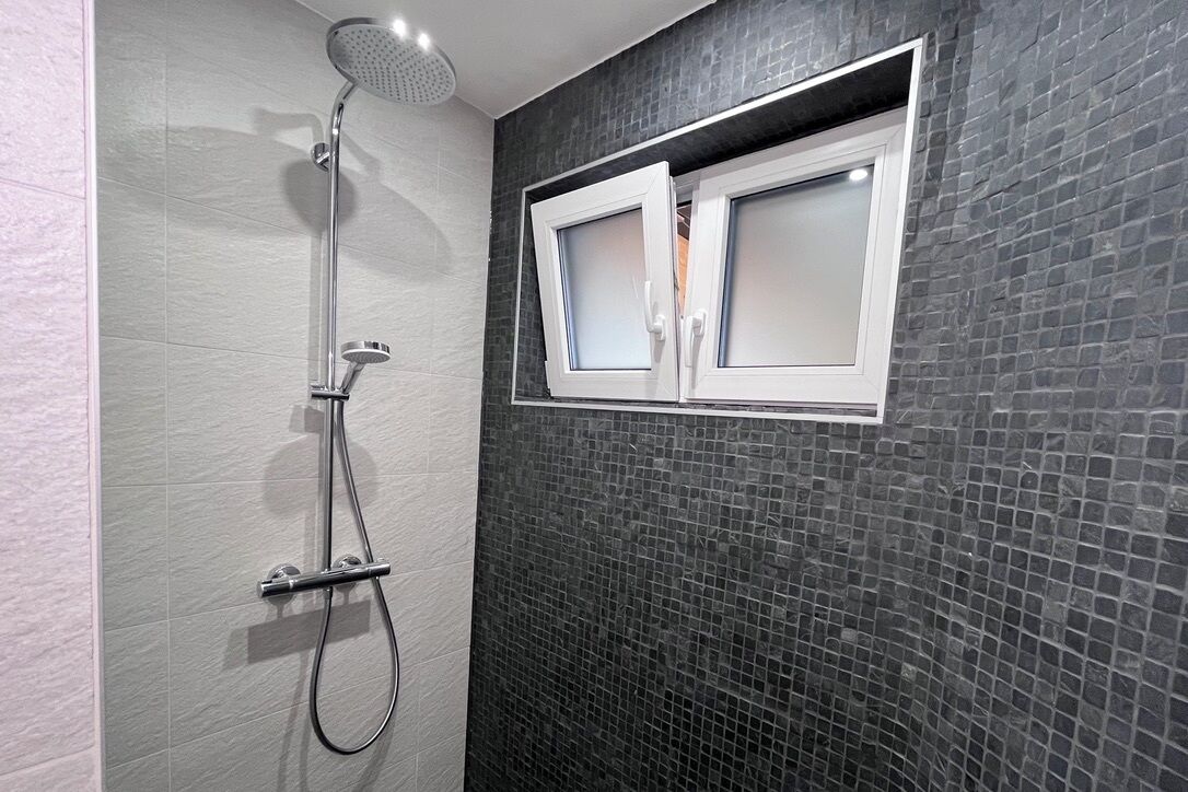 A bathroom with a shower, tiled walls, and a window with frosted glass.
