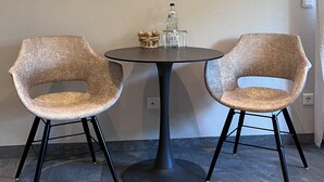 Un comedor con dos sillas y una mesa, una obra de arte en la pared y una botella sobre la mesa.