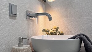 Un baño moderno con un lavabo de pedestal grande, un jabonera de piedra, una toalla y un aplique de pared.