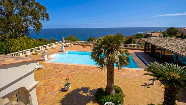 A pool area with a view of the sea, surrounded by palm trees and a tiled deck.