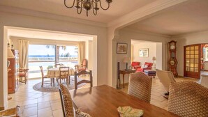 A dining area with a wooden table and chairs, a chandelier, and a view of the ocean through a glass door.