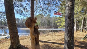 En træskulptur af en bjørn i en skov, med en sø og et amerikansk flag i baggrunden.