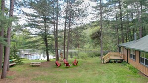 En hytte med terrasse, en anløbsbro og et picnicbord i et skovområde med en sø.