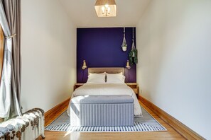 Ein Schlafzimmer mit einem großen Bett, einer Holzbänkl, einer hängenden Pflanze und einem gemusterten Teppich.