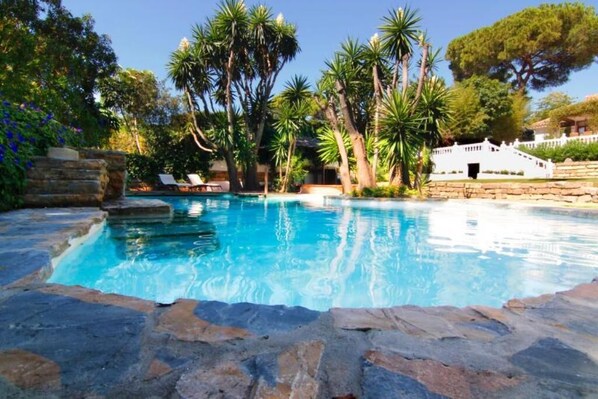 Relax by the serene pool surrounded by lush greenery and natural stone steps.