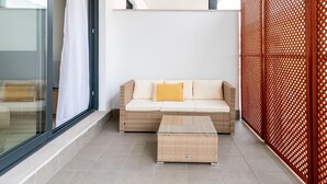 A modern balcony with a wicker sofa, a glass table, and a wooden lattice partition. - Holi-Rent Pobladores (Camas)