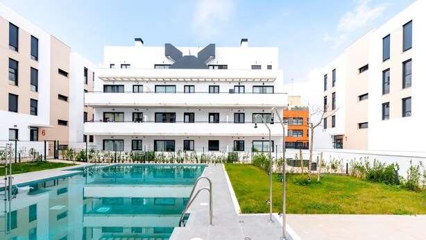 A modern building with a pool area, featuring a large pool, a covered walkway, and a well-maintained lawn. - Holi-Rent Pobladores (Camas)