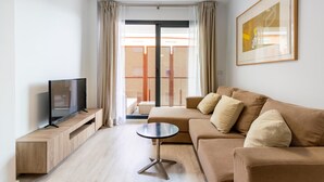 A modern living room with a sofa, a TV on a wooden stand, a round coffee table, and a balcony with a view. - Holi-Rent Pobladores (Camas)