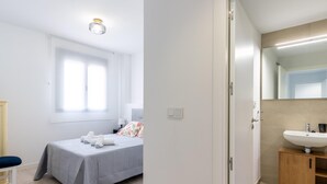 A bedroom with a bed, bedside table, and a window. - Holi-Rent Pobladores (Camas)
