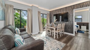 Ein modernes Wohnzimmer mit einer Couch, einem Esstisch und Stühlen. Ein Fernseher ist an der Wand montiert und es gibt ein Fenster mit Vorhängen.