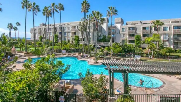 Ein Hotel mit großem Swimmingpool, umgeben von Palmen und einer Liegefläche.