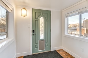 Una puerta verde con un panel de vidrio, una lámpara encima y una ventana a la derecha.