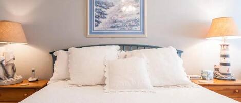 A neatly made bed with white linens and pillows, a framed artwork above it, and two bedside lamps on wooden nightstands.
