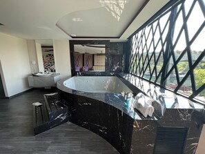 Une salle de bain moderne avec une grande baignoire, un meuble-lavabo et une grande fenêtre donnant sur la ville.