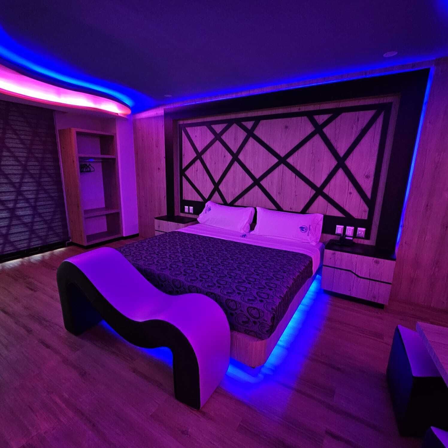 A modern bedroom with a wooden headboard, a patterned bedspread, and a bench.