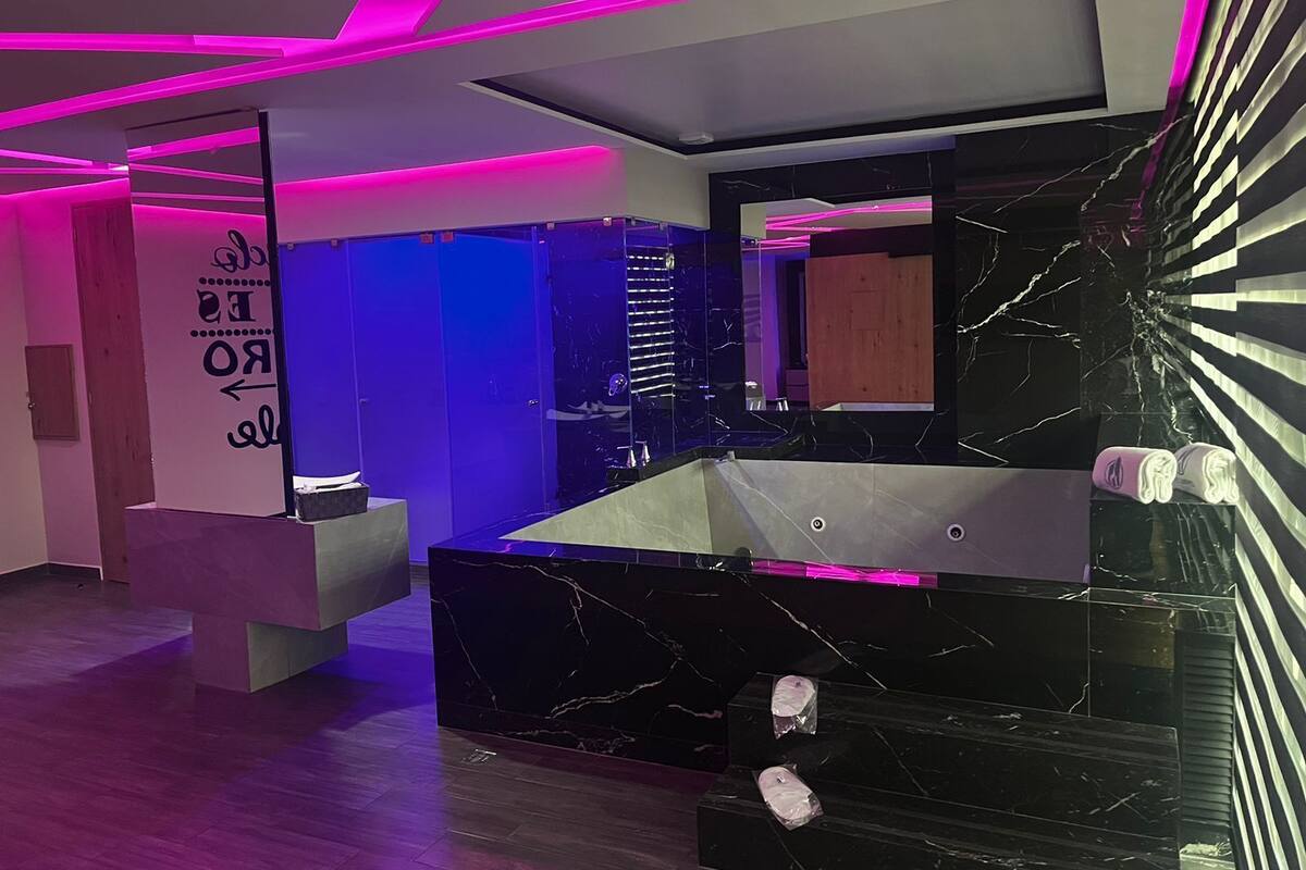Une salle de bain moderne avec un lavabo en marbre noir, un grand miroir et des éléments d’éclairage aux nuances roses.