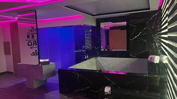 A modern bathroom with a black marble sink, a large mirror, and pink lighting accents.