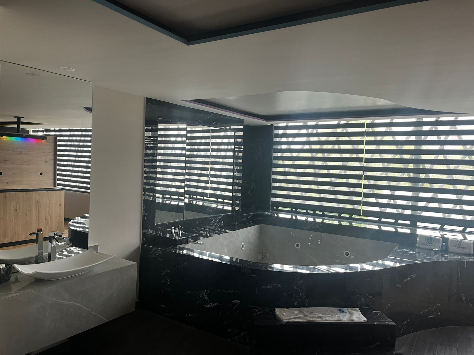 Un baño moderno con una amplia bañera de mármol negro, un tocador de madera y un espejo grande.