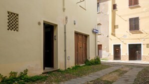 A narrow street with buildings on either side, featuring a small entrance with a wooden door and a window with shutters. - Catalan Loft Retreat (Alghero)