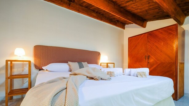A neatly made bed with white linens, two bedside tables with lamps, and a wooden wardrobe. - Catalan Loft Retreat (Alghero)